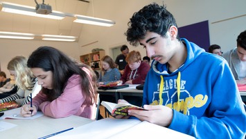 En elev läser och andra elever skriver i ett klassrum