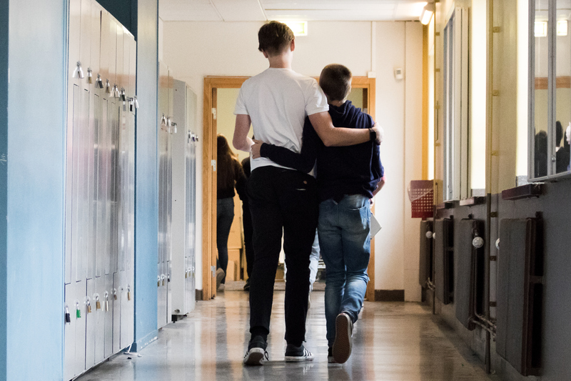 två elever går i skolkorridoren och håller om varandra