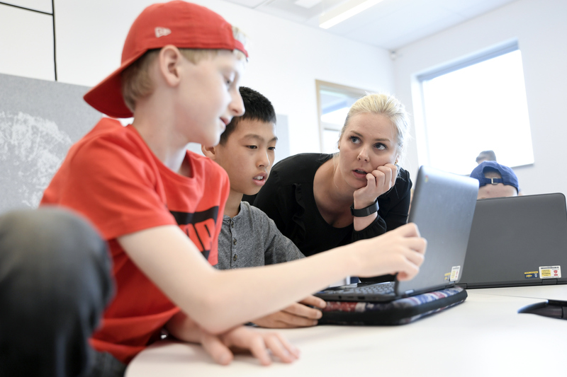 Lärare diskuterar med två elever som jobbar med datorn