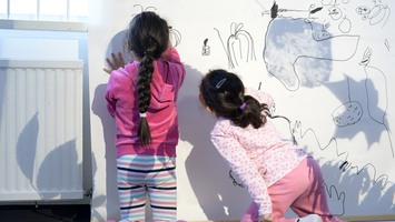 Två barn på förskolan ritar på ett papper där det projiceras löv och annat naturmaterial