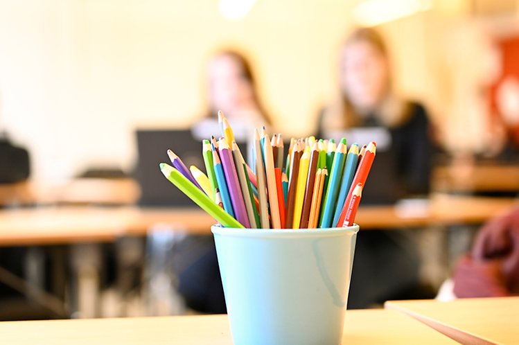 Pennställ med färgglada pennor i klassrum och elever syns suddigt i bakgrunden